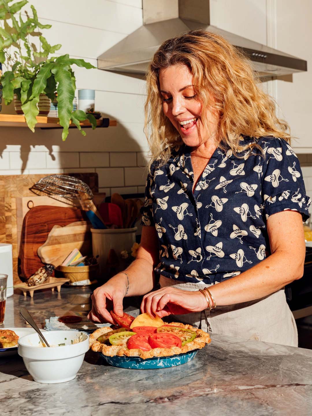 Woman preparing a vegetable tart with sliced tomatoes and cucumbers in a kitchen