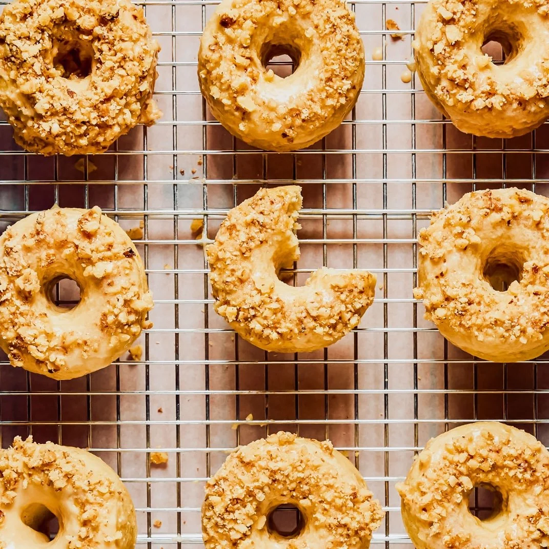 Nine glazed donuts with crumb topping on a cooling rack, with one donut partially eaten.