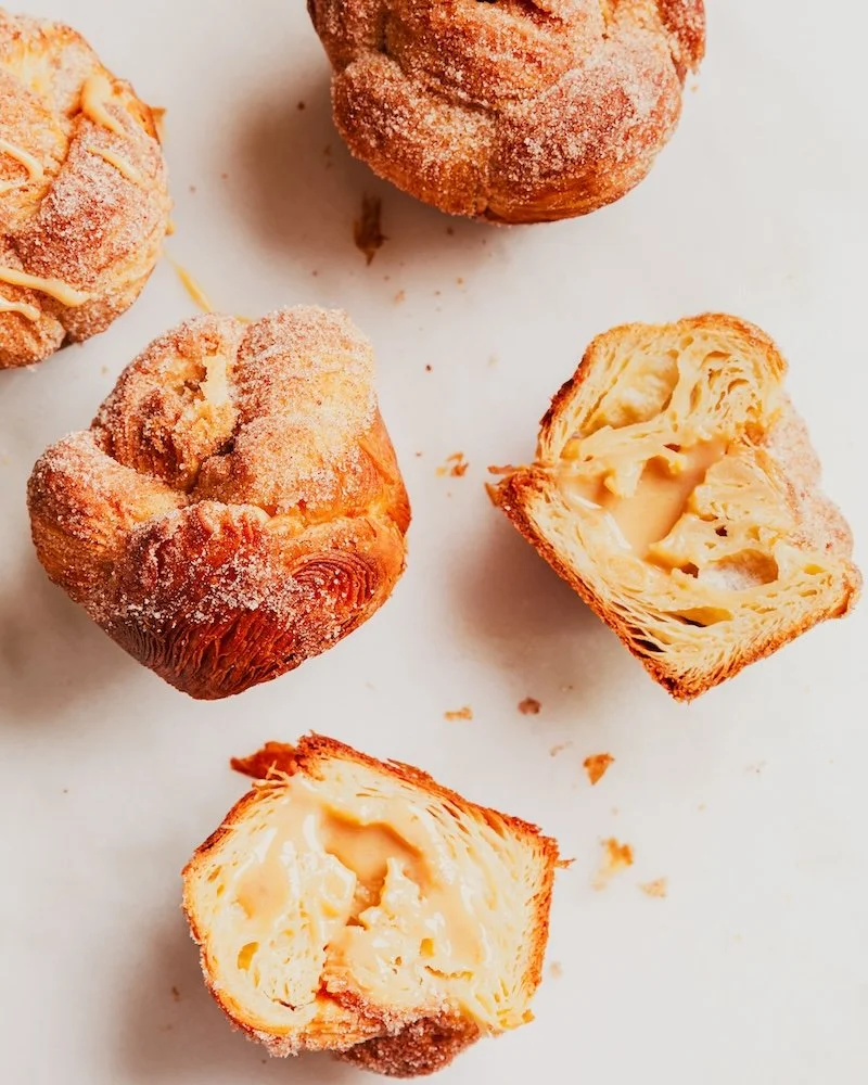 Close-up of three sugar-dusted cream-filled pastries with two cut open to reveal creamy filling inside.