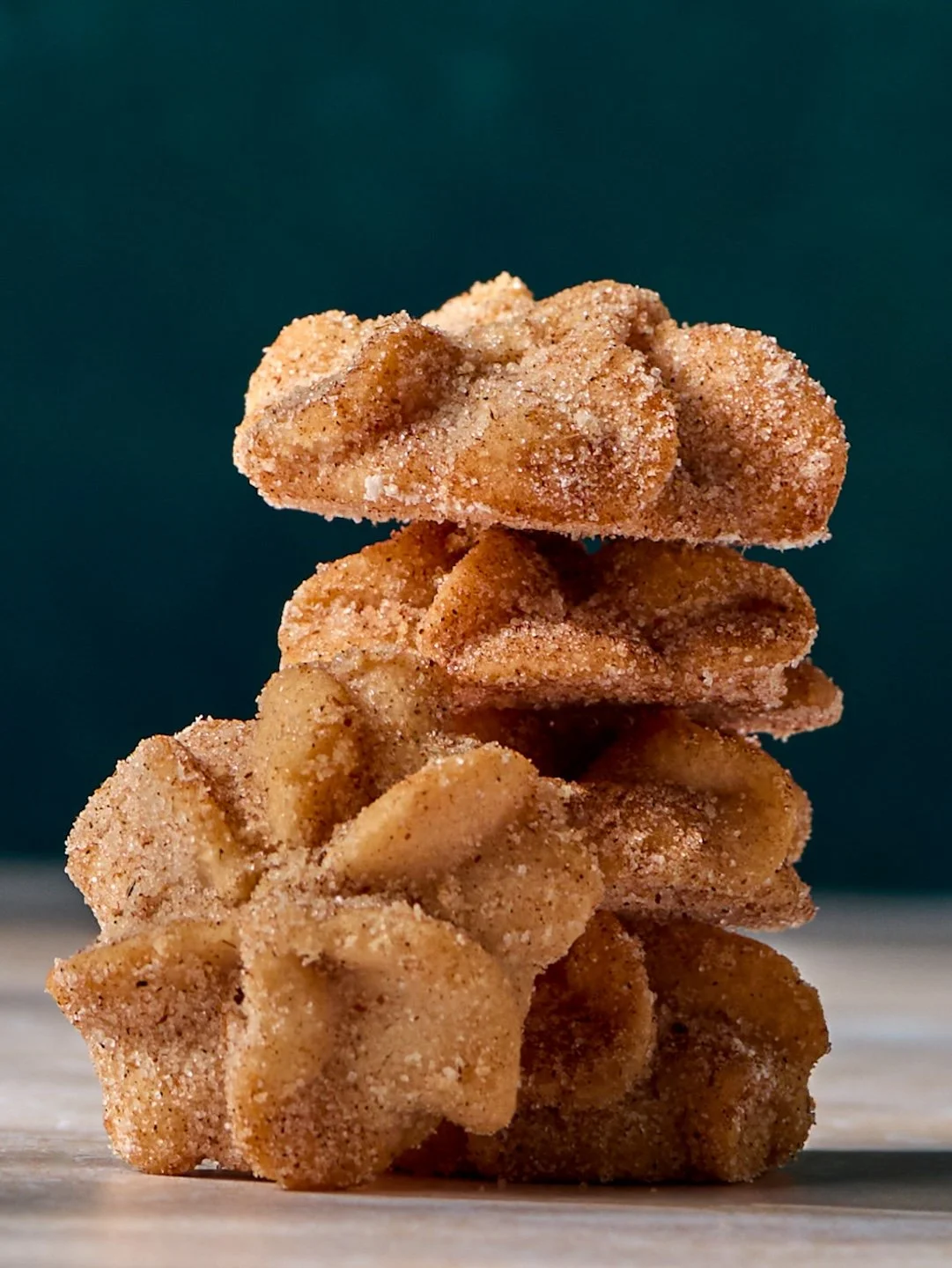 Stack of powdered sugar-coated fried dough cookies against dark background.