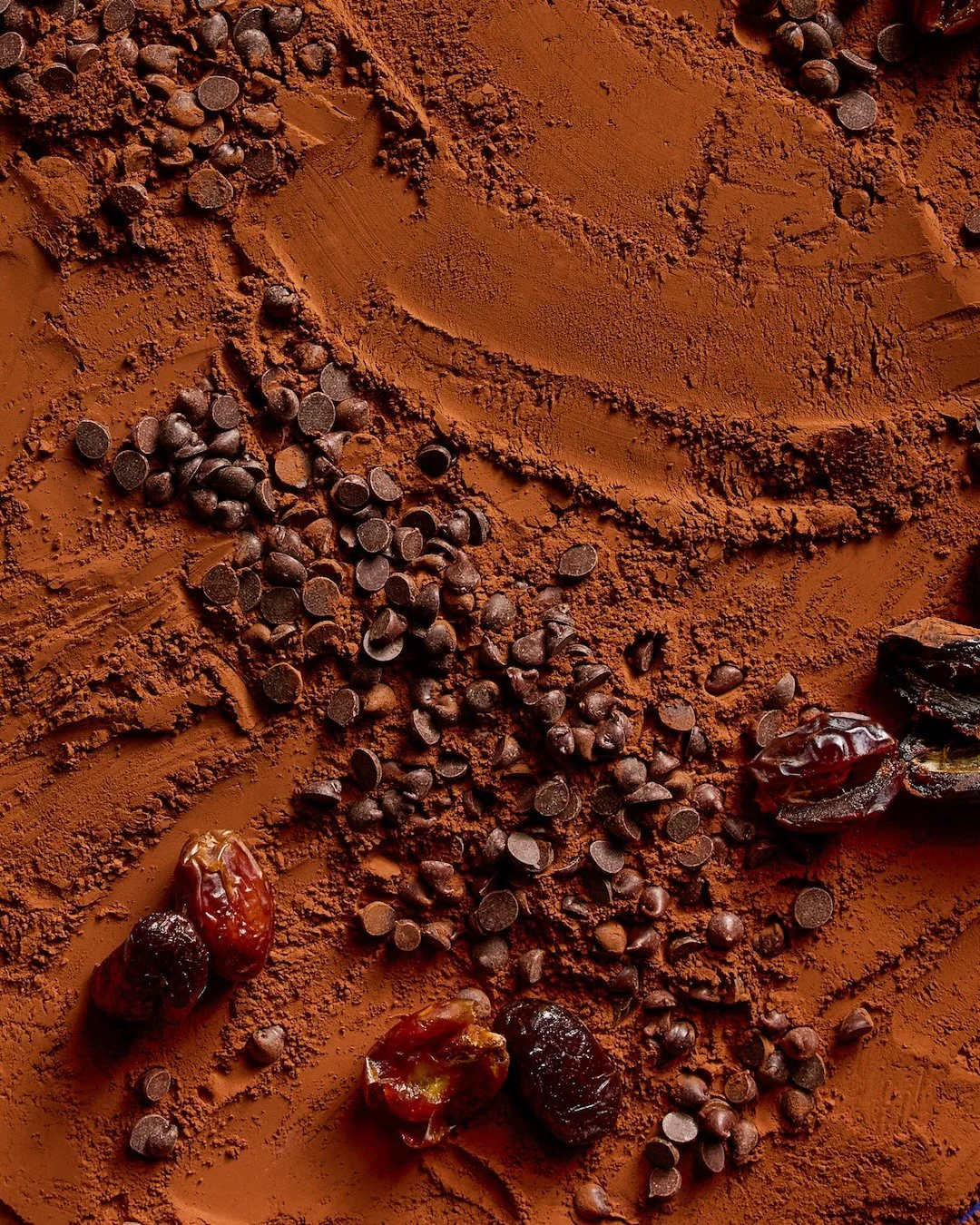Close-up of cocoa powder sprinkled on a surface with scattered chocolate chips and dates.