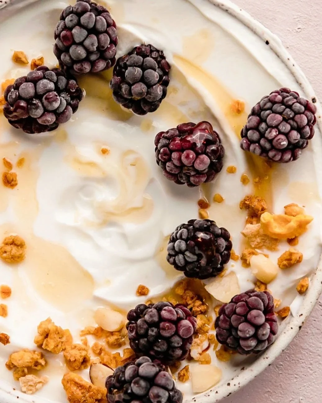 Close-up of a dessert topped with blackberries, white cream, caramel drizzle, and chopped nuts.