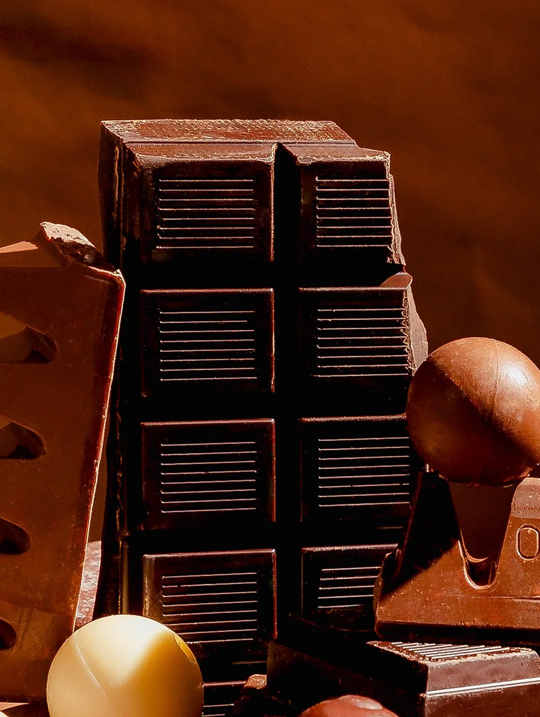 Close-up view of various pieces of dark chocolate with different shapes and textures, some with grooves, and some spherical, arranged against a dark background.