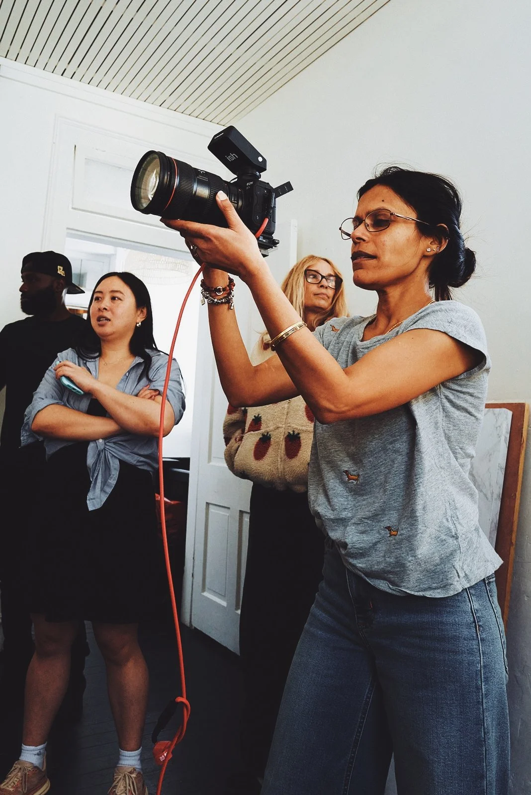 A woman holding a professional camera with a flash attachment, surrounded by several people indoors.