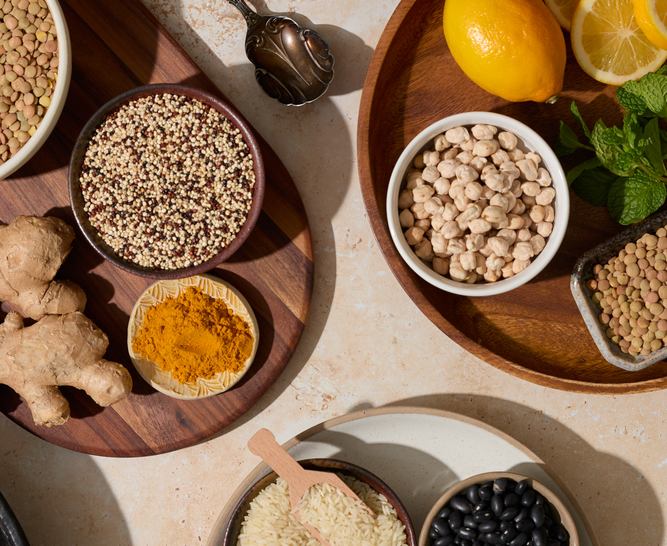 Assorted spices, grains, and legumes on wooden and ceramic dishes, with lemons and fresh mint.