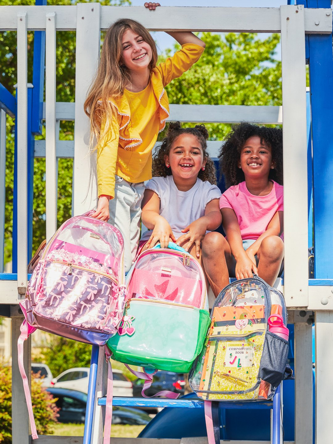 Four smiling girls with backpacks on a playground.