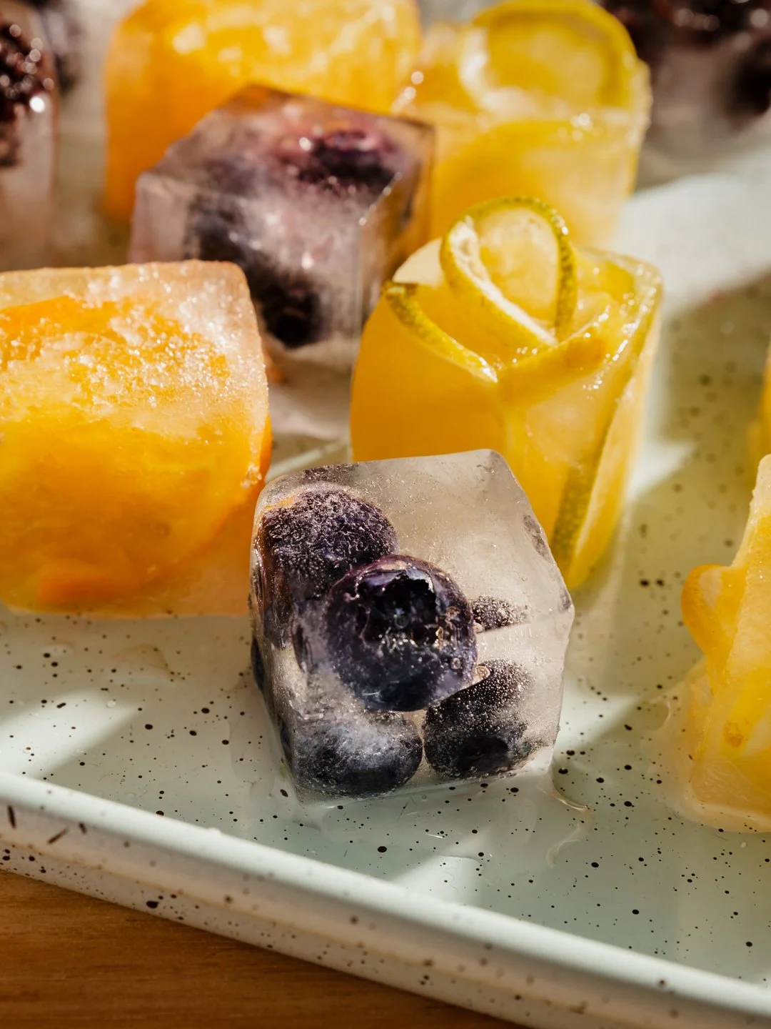 Close-up of mixed citrus fruit slices and blueberries frozen in ice cubes.