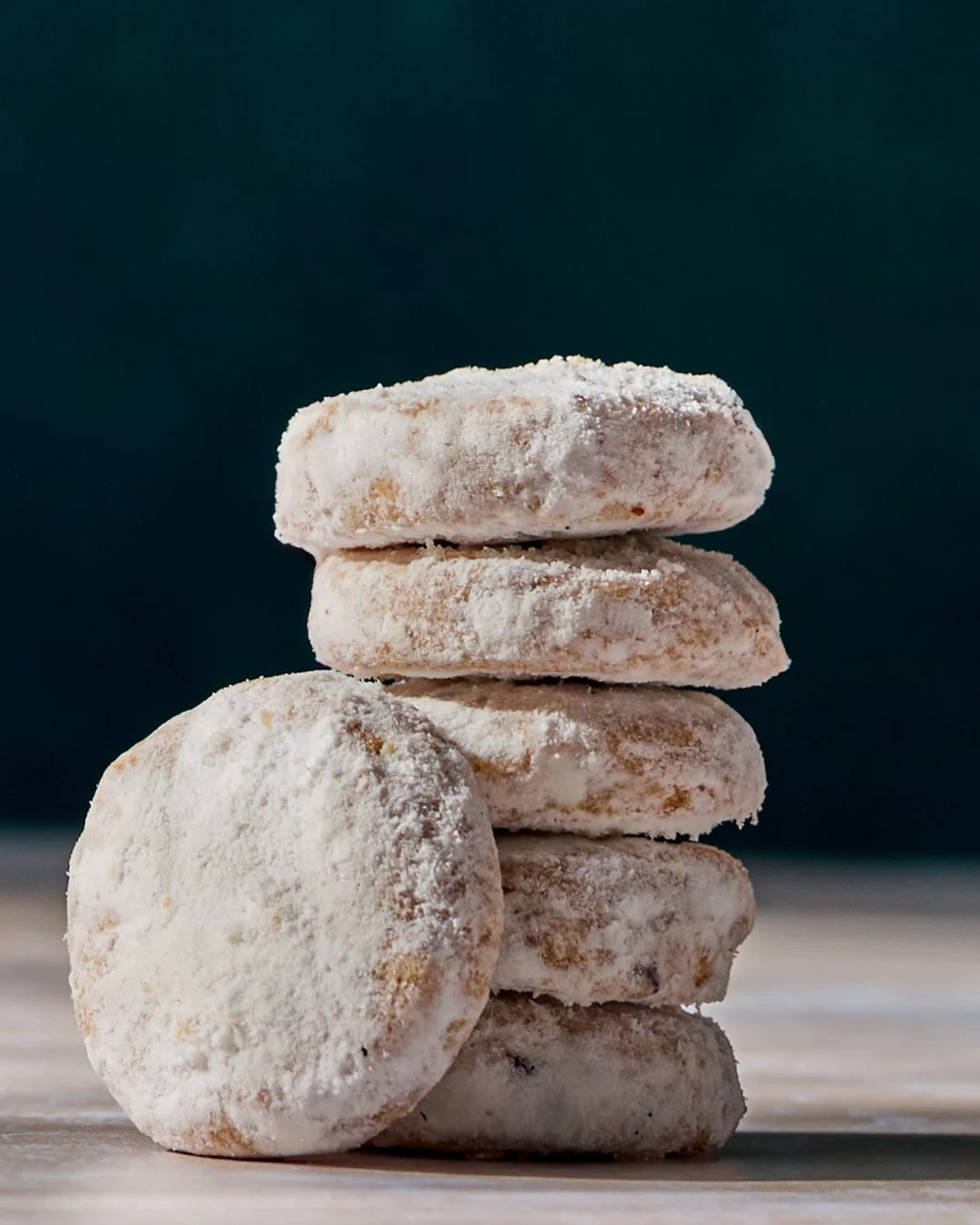 A stack of five powdered sugar-dusted cookies on a light surface with a dark background.