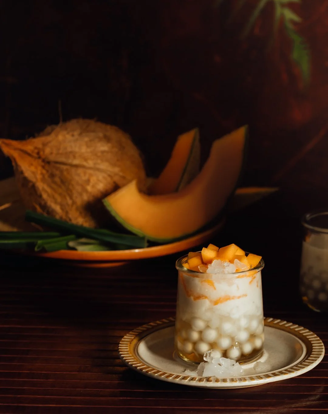 Dessert in a glass topped with diced mango, with tapioca pearls and cream inside, on a decorative plate.