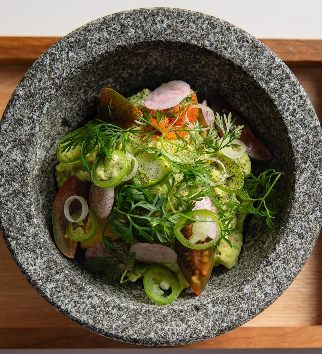 A bowl of chopped vegetables topped with microgreens, sliced radishes, cherry tomatoes, and pepper.