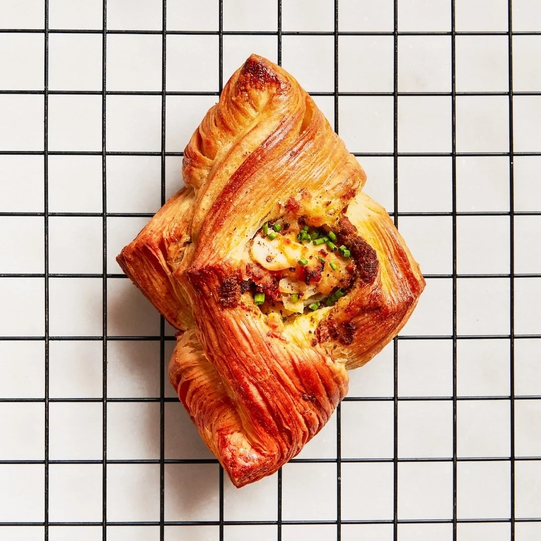 A savory pastry with a golden, flaky crust, filled with cheese, vegetables, and herbs, placed on a wire cooling rack.