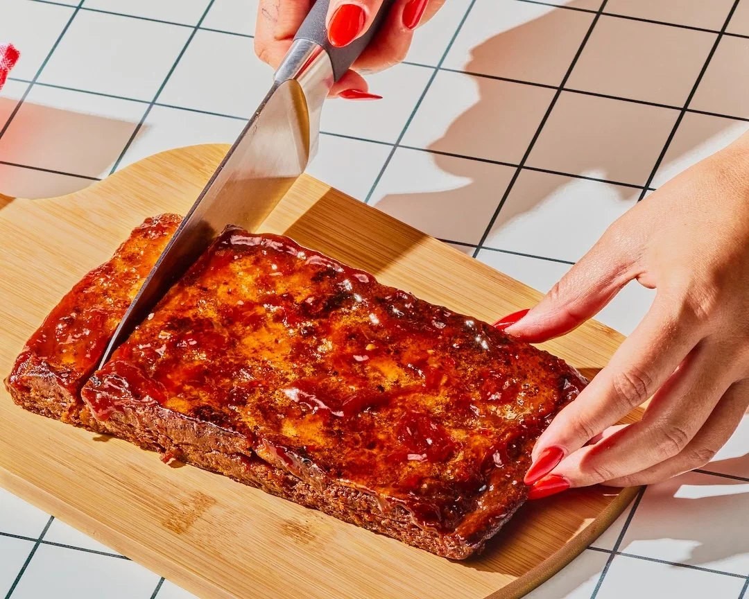 Person slicing a cooked rack of barbecue ribs on a wooden cutting board.