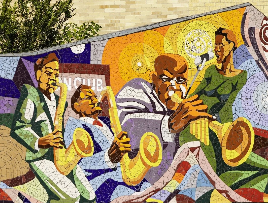 Colorful mosaic mural of jazz musicians playing instruments such as a trumpet, saxophone, and clarinet, with a vibrant background.