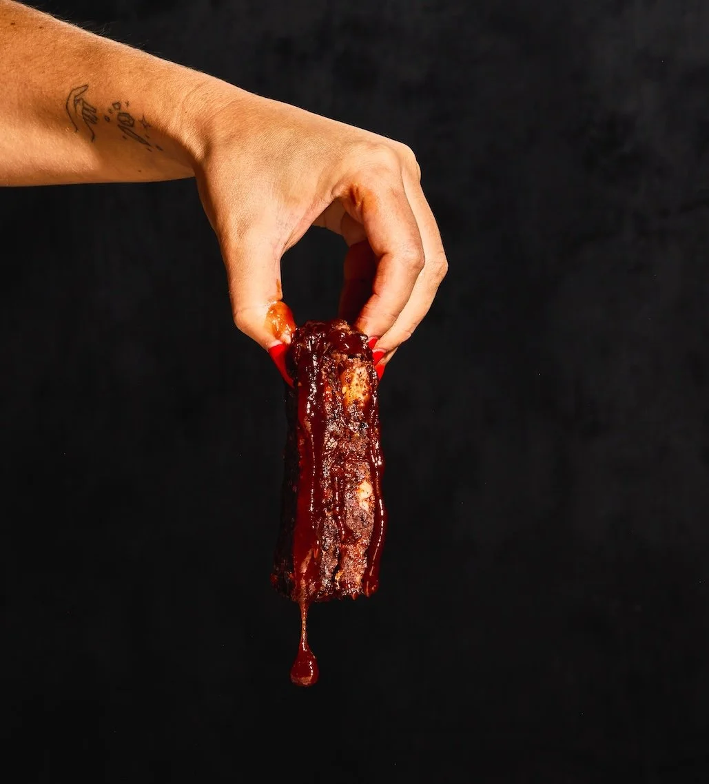 A person holding a piece of glazed bacon with a dark background.