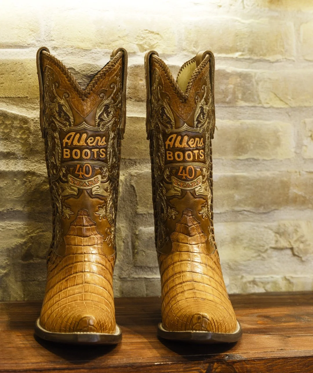 Pair of cowboy boots with intricate embroidery, celebrating Allen's 40th anniversary, against a brick wall background.