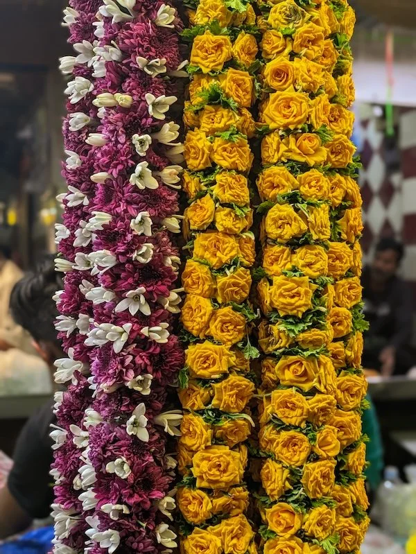 Close-up of three vertical floral garlands featuring purple and white orchids on the left, and yellow roses with green leaves on the right.