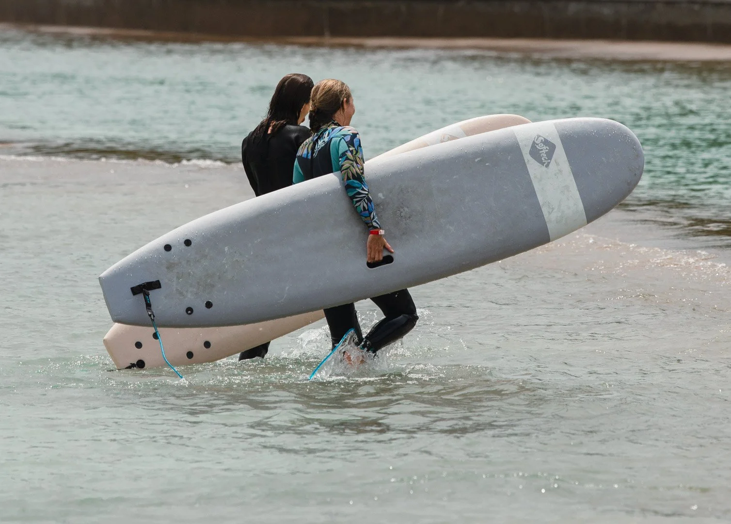 Two women heading into the water with surfboards at a beach.