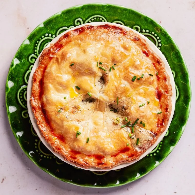 Baked egg casserole topped with melted cheese and garnished with chopped green herbs, served on a green decorative plate.