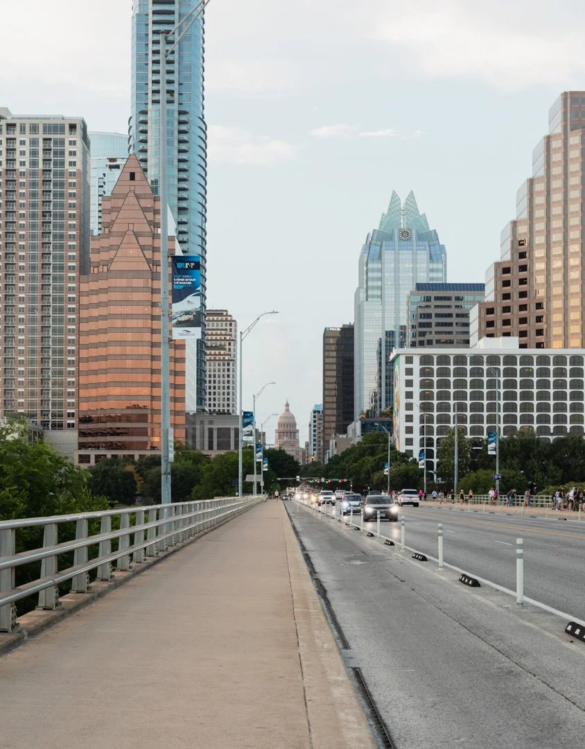 City skyline with tall buildings, a bridge with cars, and the Texas State Capitol building in the distance in Austin, Texas.
