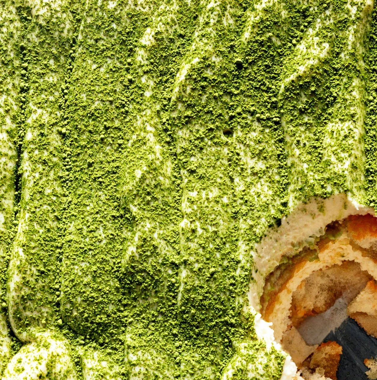 Close-up of a green matcha-flavored Swiss roll cake with textured green sponge and visible layers of cream and cake inside.