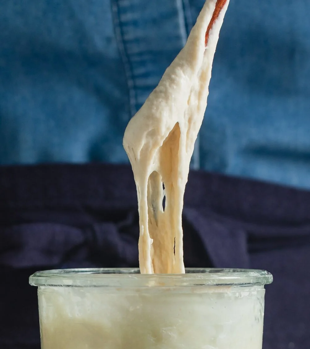 Close-up of melted cheese stretching from a spoon into a glass container of cheese dip.