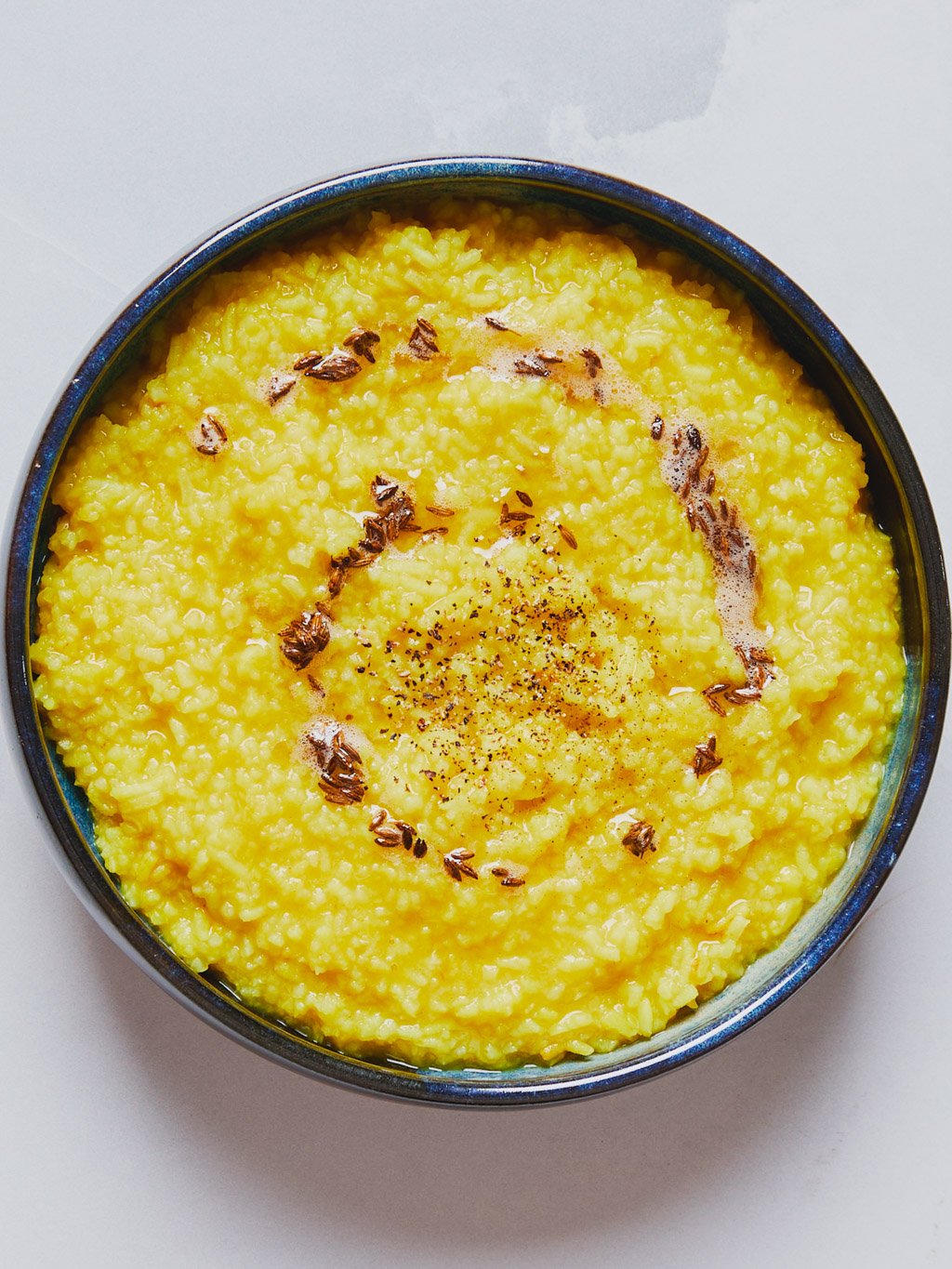 A bowl of yellow polenta topped with black pepper, herbs, and spices.
