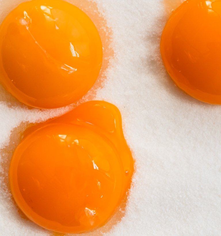 Close-up of three raw egg yolks on white salt or sugar granules.