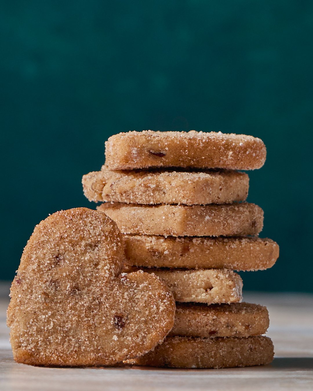 Stack of sugar-coated cookies on a wooden surface, with one cookie leaning against the stack, against a dark teal background.