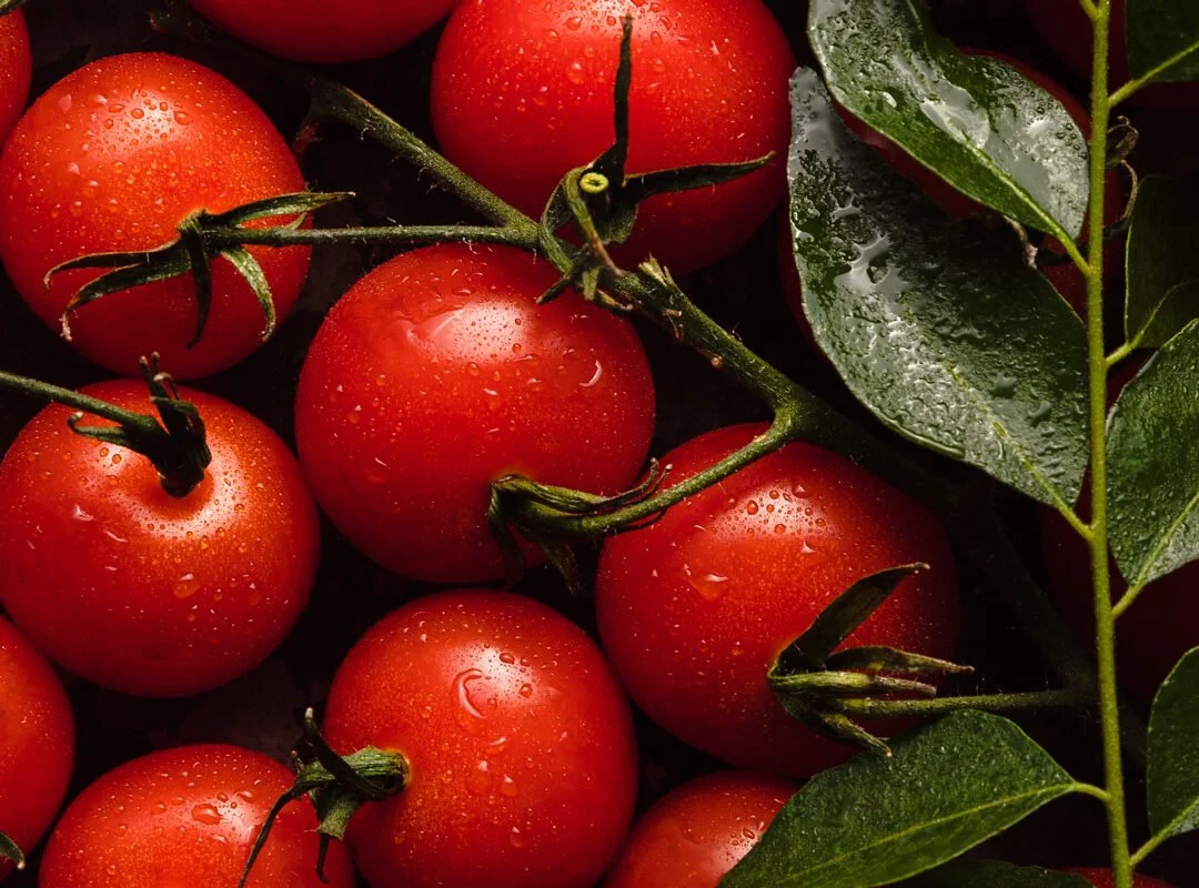 Cluster of ripe red tomatoes with water droplets on their surface, accompanied by green leaves.