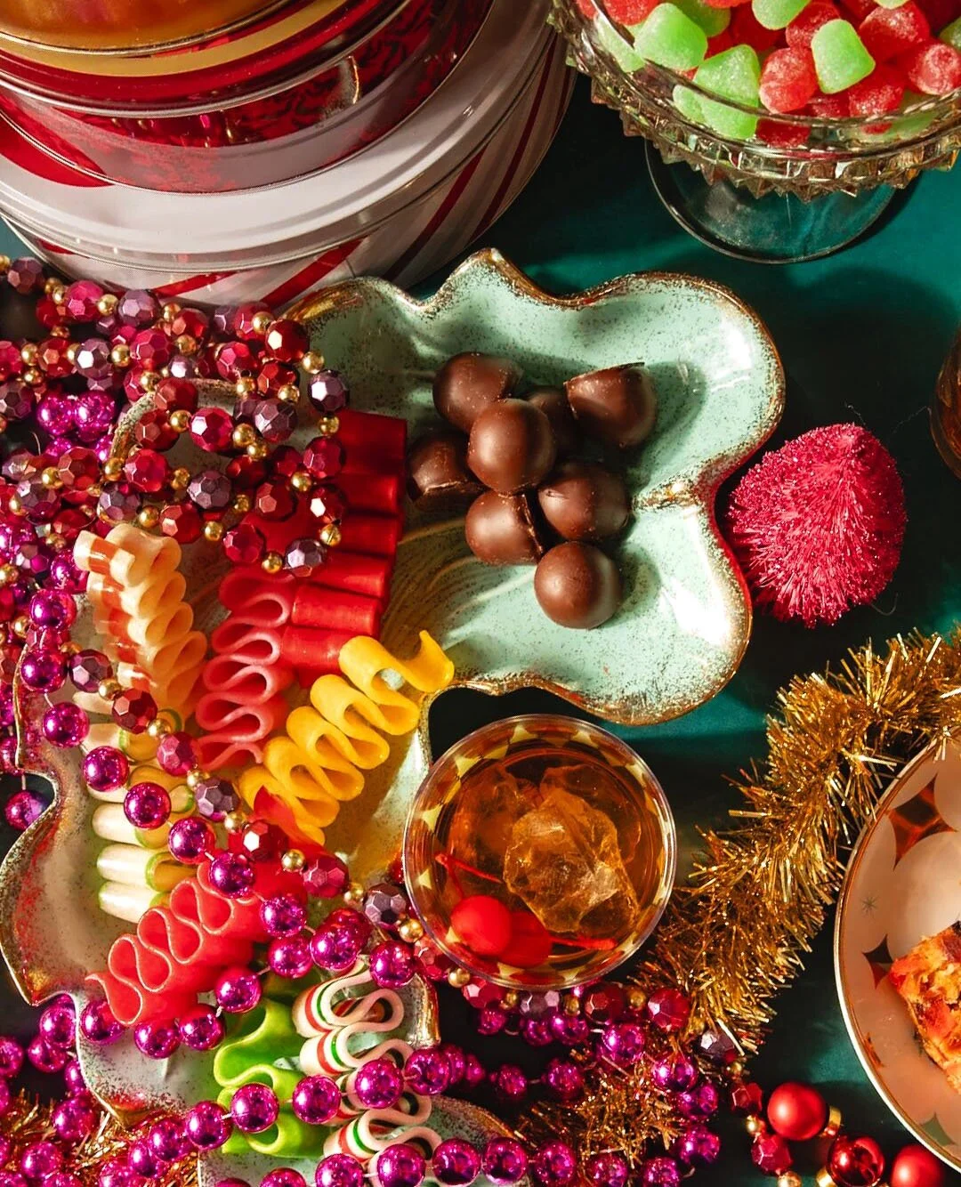Festive holiday table with colorful candies, chocolates, and Christmas decorations including beads, tinsel, and bowls of treats.