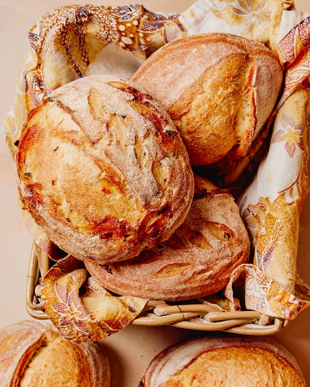 Basket of freshly baked bread rolls, some with a crusty exterior, lined with a decorative patterned cloth.