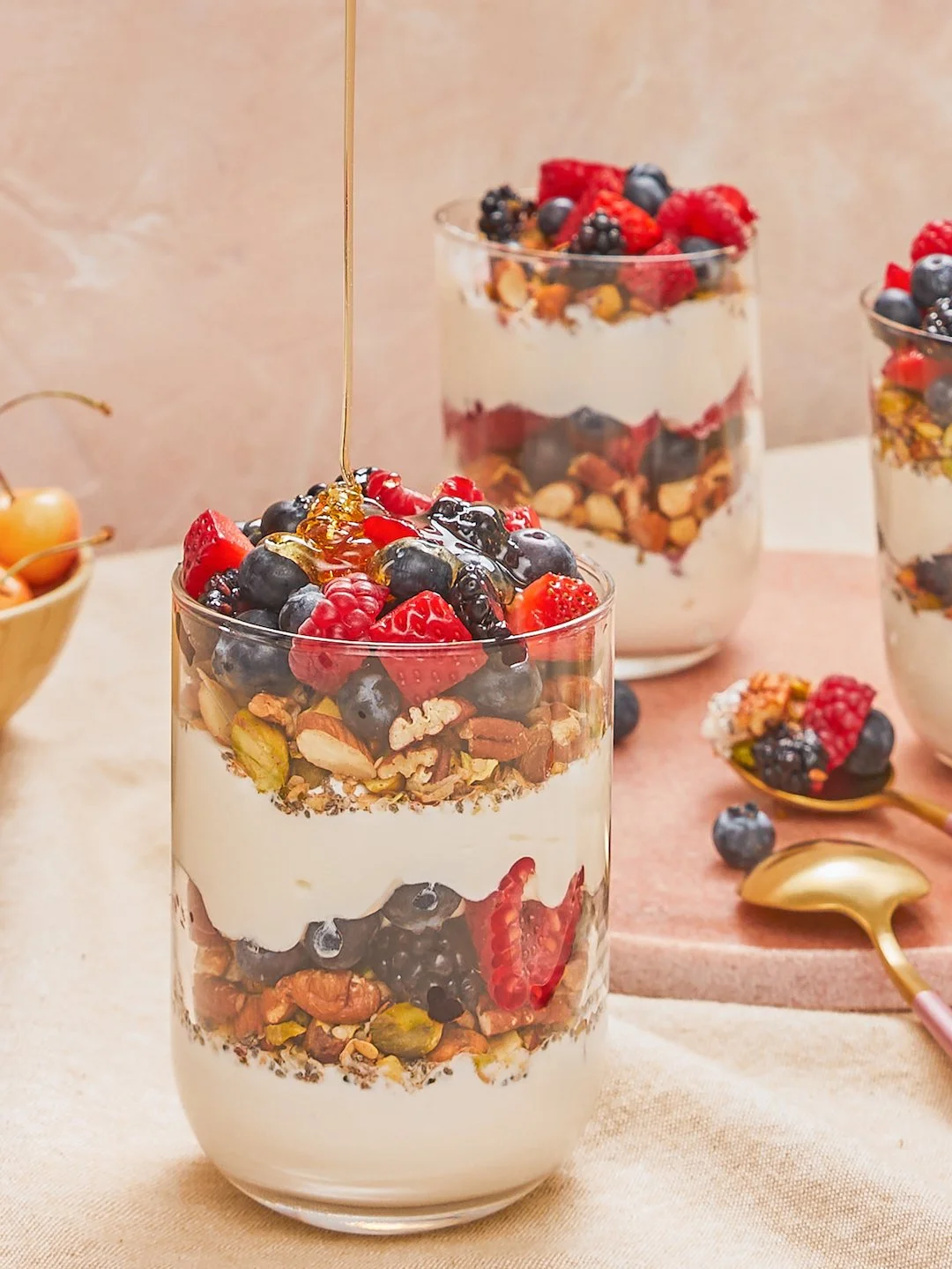 A layered yogurt parfait with granola, mixed berries, and honey in a clear glass.