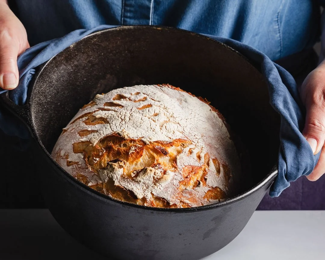 Baked bread in a black cast iron Dutch oven, with a flour-dusted crust.