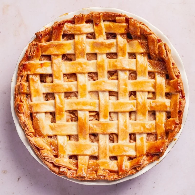 A freshly baked apple pie with a golden lattice crust on top, sitting on a white plate.