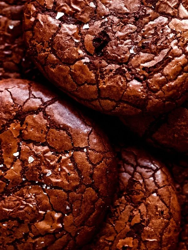 Close-up of several cracked, dark chocolate cookies with salt crystals.