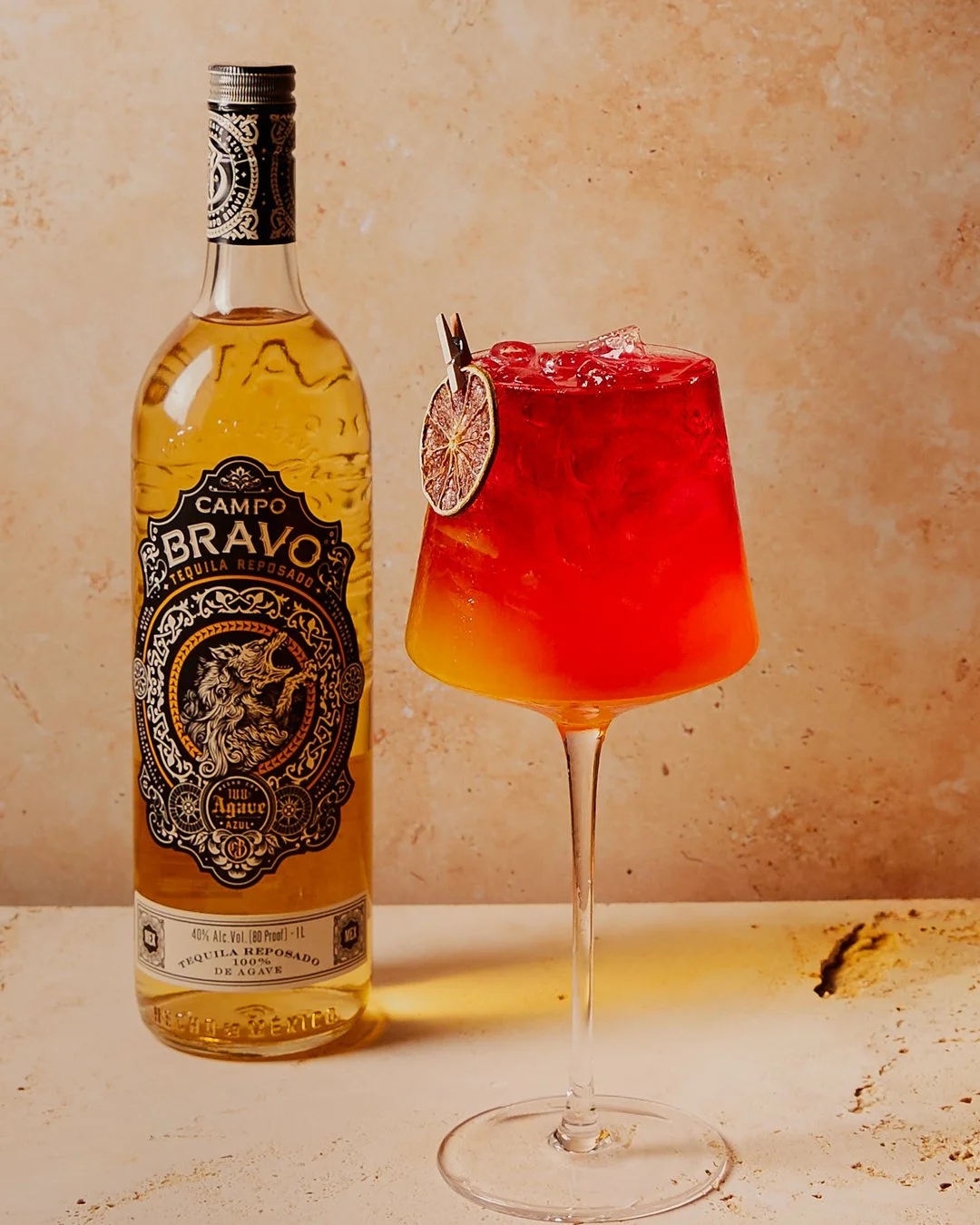 A bottle of Campo Bravo tequila and a colorful cocktail in a wine glass garnished with a dried lime slice.