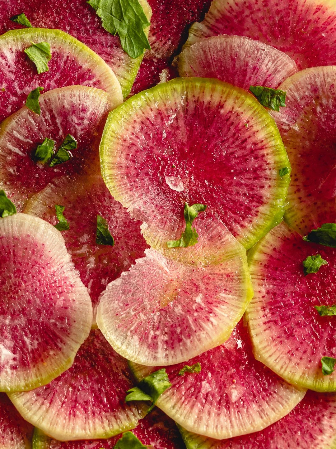 Slices of pink and green watermelon radish garnished with chopped green herbs.