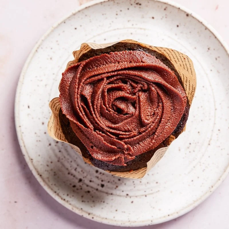 Chocolate cupcake with pink frosting swirl on top, placed on a white speckled plate.
