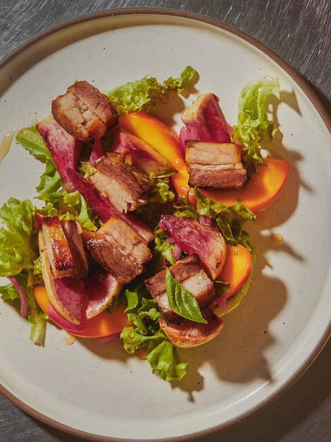 Salad with mixed greens, sliced peaches, cherry tomatoes, red onions, basil leaves, and sliced grilled pork belly.