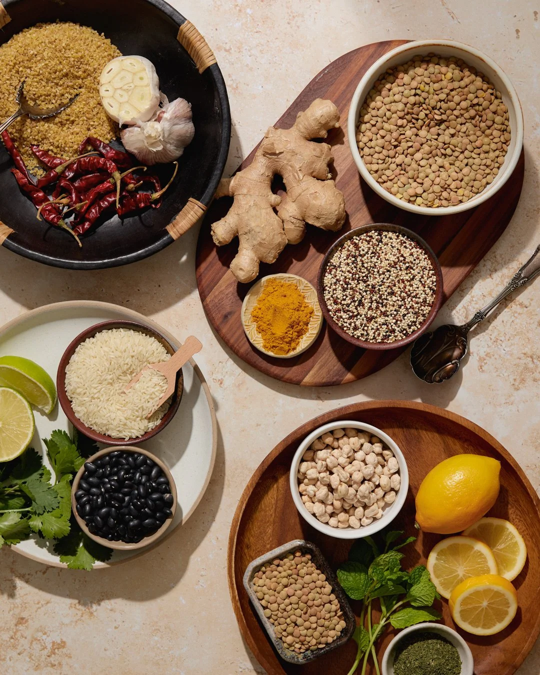 Assorted spices, herbs, legumes, lemon, garlic, ginger, rice, and chili peppers arranged on wooden and ceramic dishes.