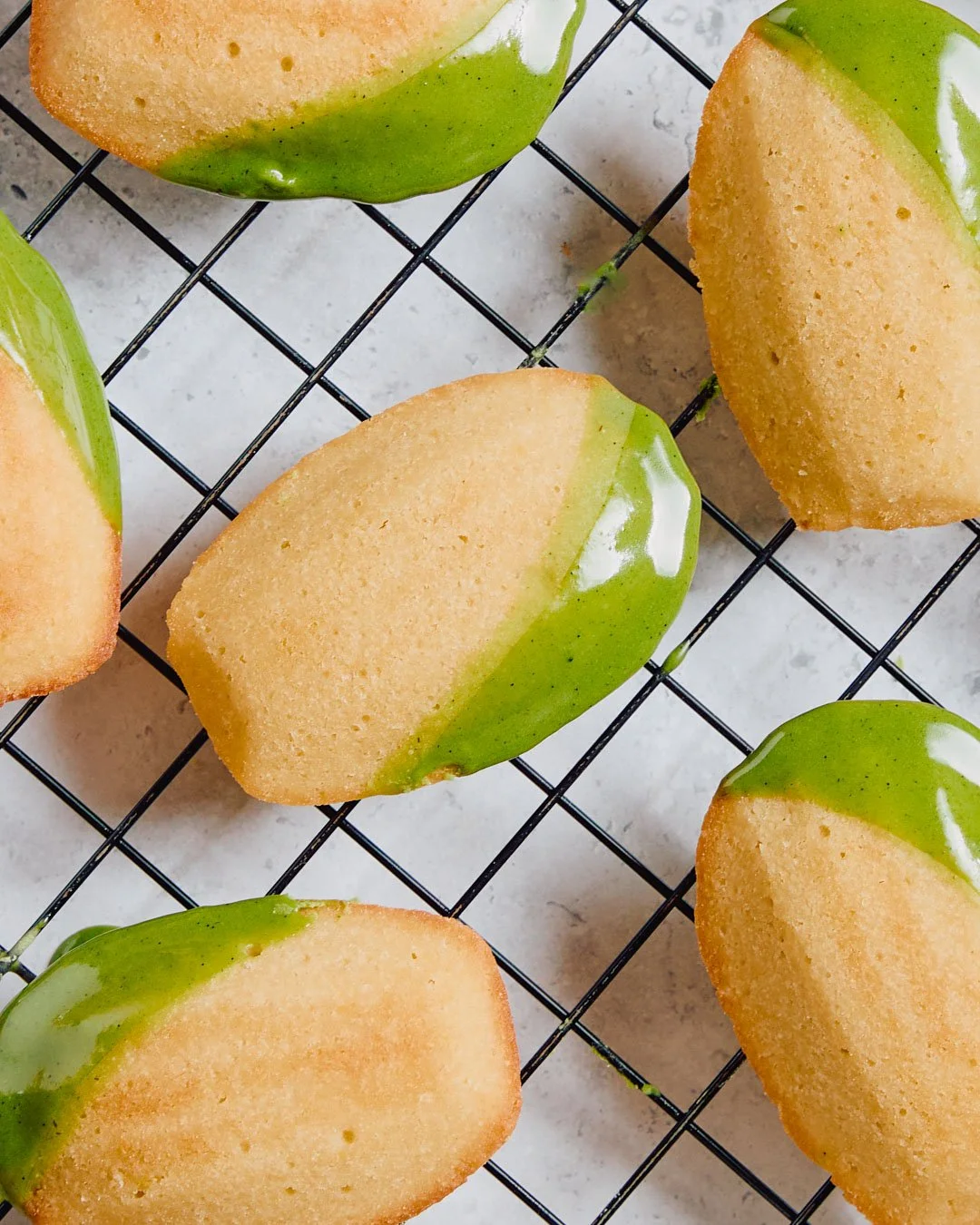 Close-up of partially dipped lemon cookies with green glaze on a wire cooling rack.