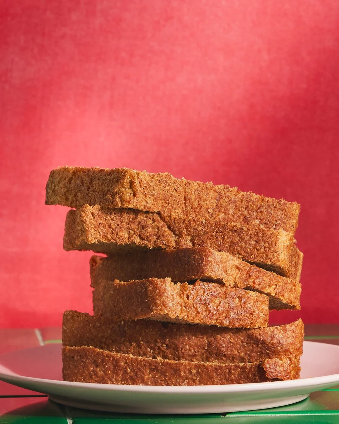 Stack of six slices of toasted bread on a white plate against a pink background.