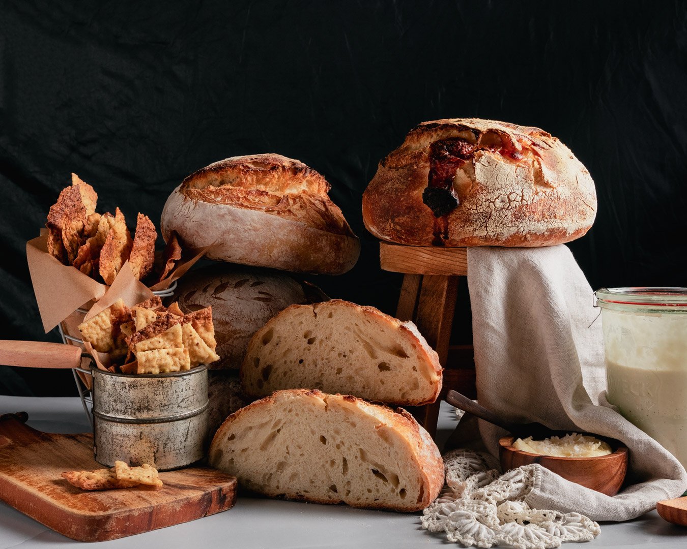 Various loaves of bread, crackers, and toppings on a table with a dark background.