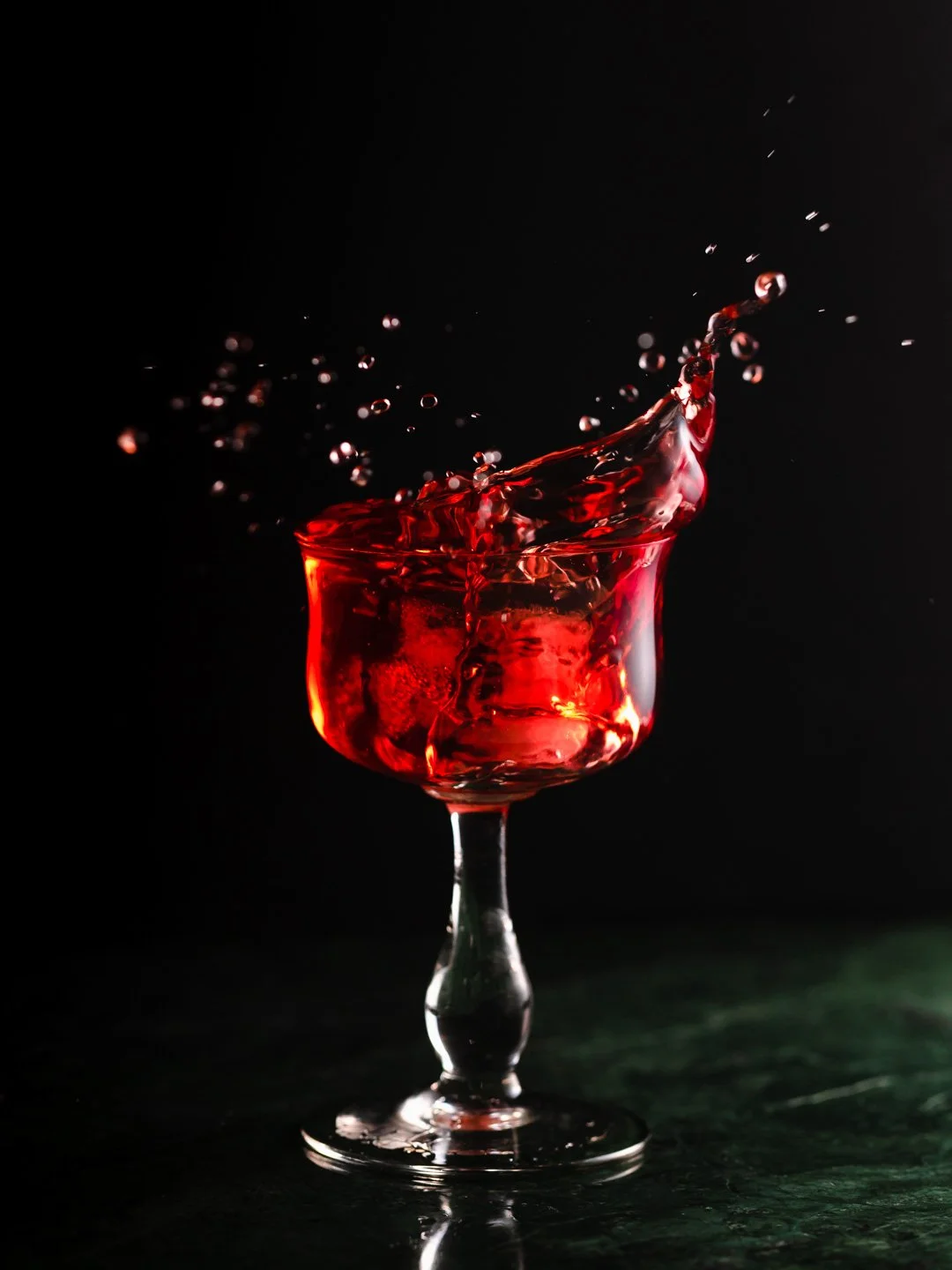 Red liquid splashing out of a glass with a dark background.