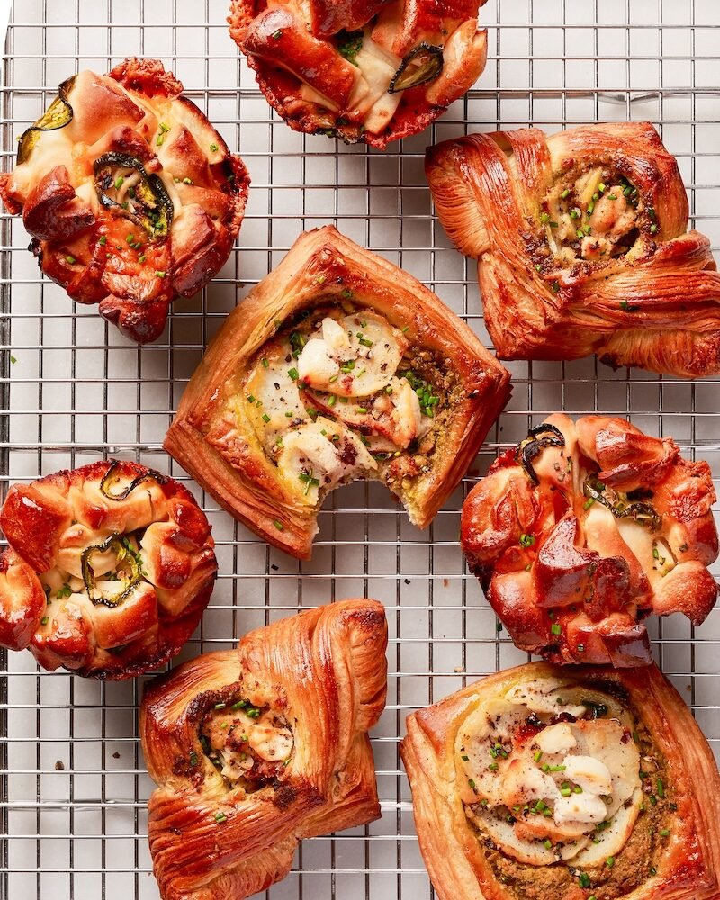 Assorted savory baked pastries with various toppings and fillings, cooling on a wire rack.