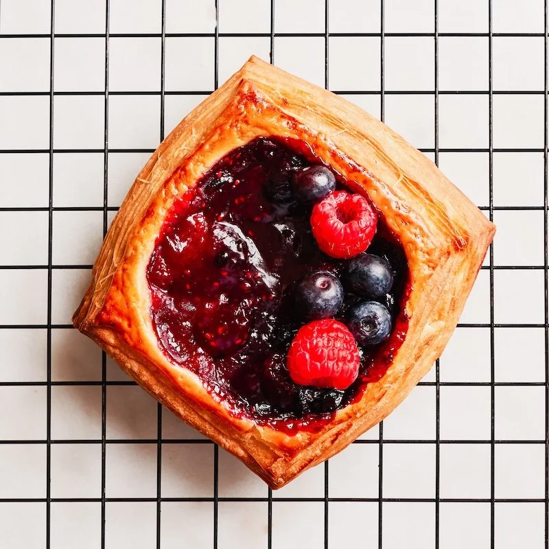 A square blueberry and raspberry pastry with a flaky crust on a cooling rack.