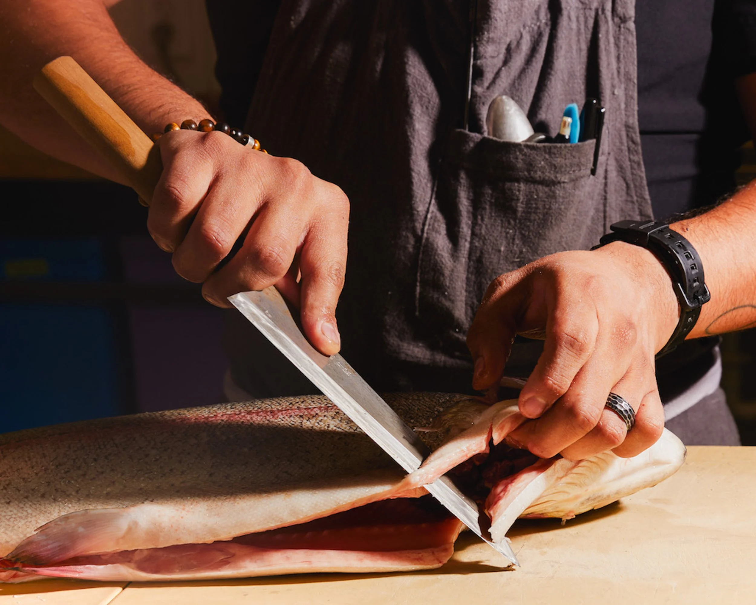 Person cleaning and preparing a fish on a cutting board, with various pens and tools in the shirt pocket.