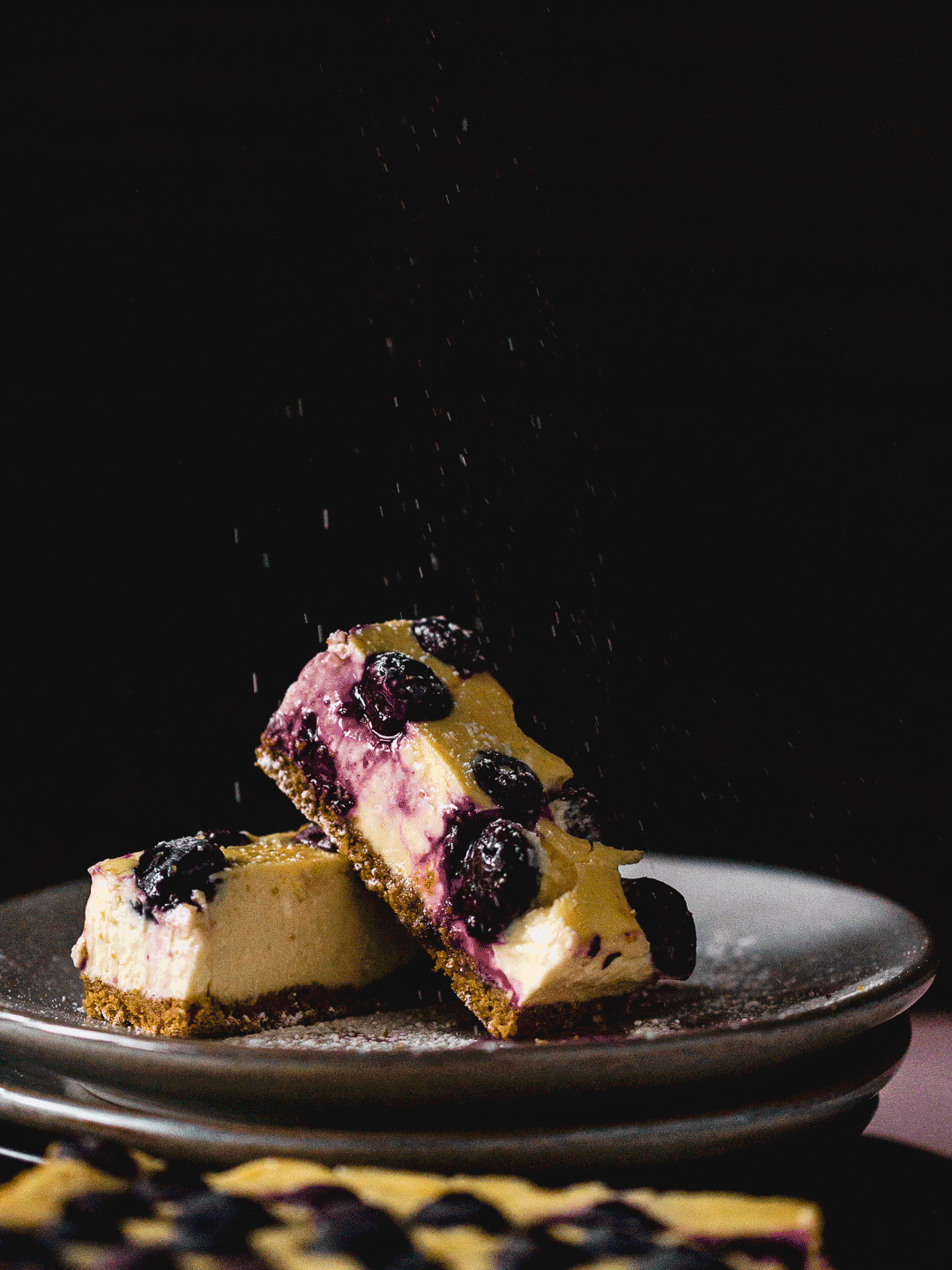 Slices of blueberry cheesecake on a dark plate.