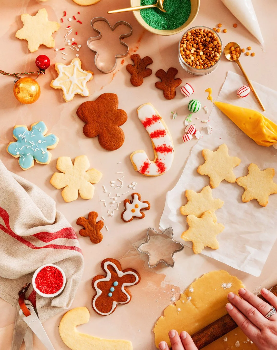A table with various decorated Christmas cookies, cookie cutters, sprinkles, frosting, and candy, in a festive holiday setting.