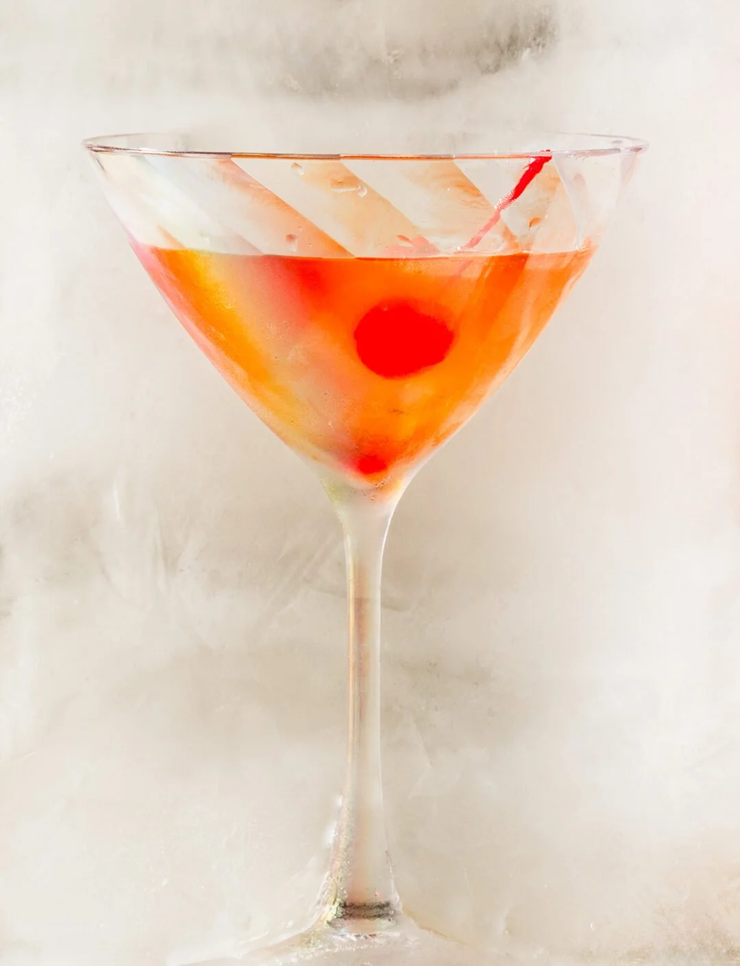 A classic pink cocktail in a martini glass garnished with a cherry and a decorated cocktail umbrella.